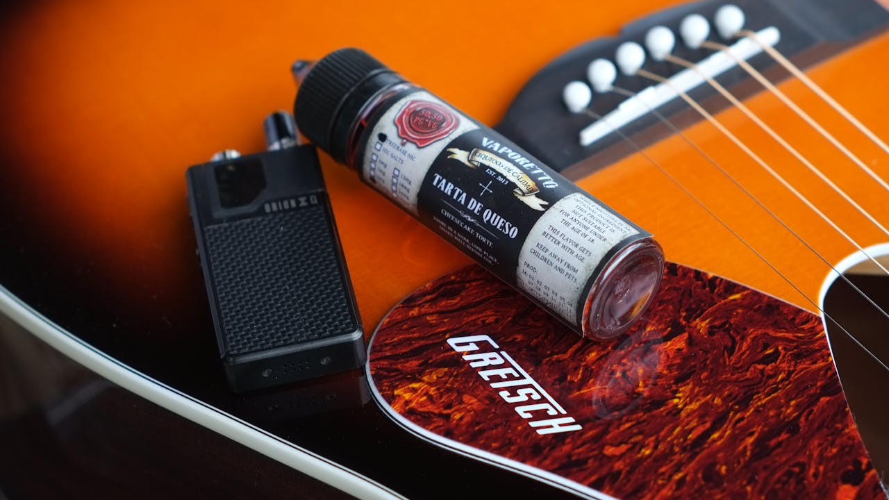 A vape device and e-liquid bottle on an acoustic guitar surface with a Gretsch pickguard.