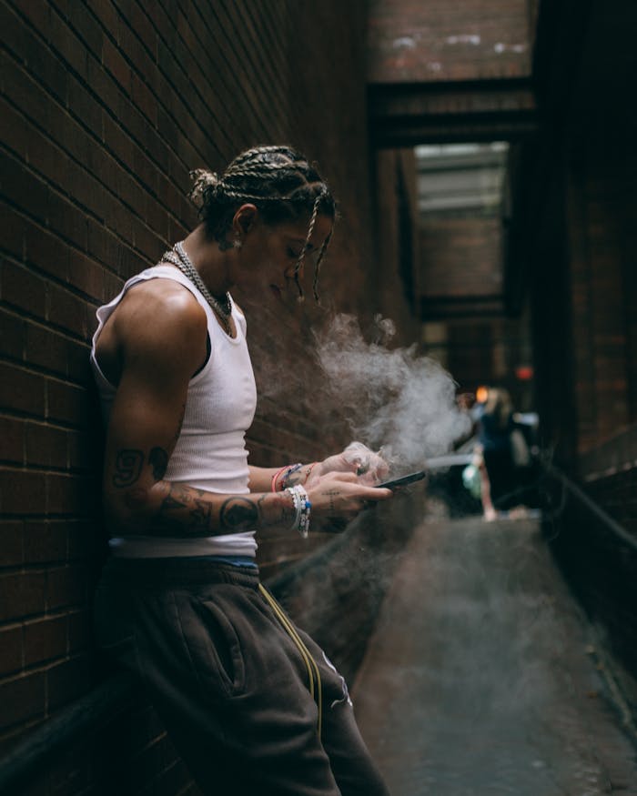 Young adult with tattoos smoking in a narrow urban alleyway, creating an edgy atmosphere.
